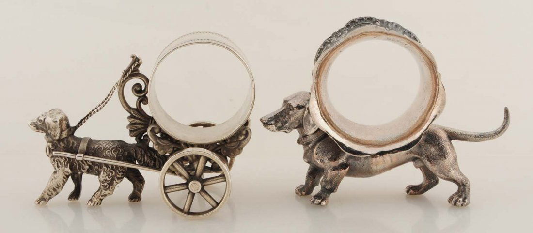 Lot of 2: Figural Napkin Rings.: The first napkin ring has a proud little dog pulling a napkin holder on wheels. The mark is difficult to read, but 'No. 033' is visible. The second napkin ring has a handsome dachshund carrying a scal