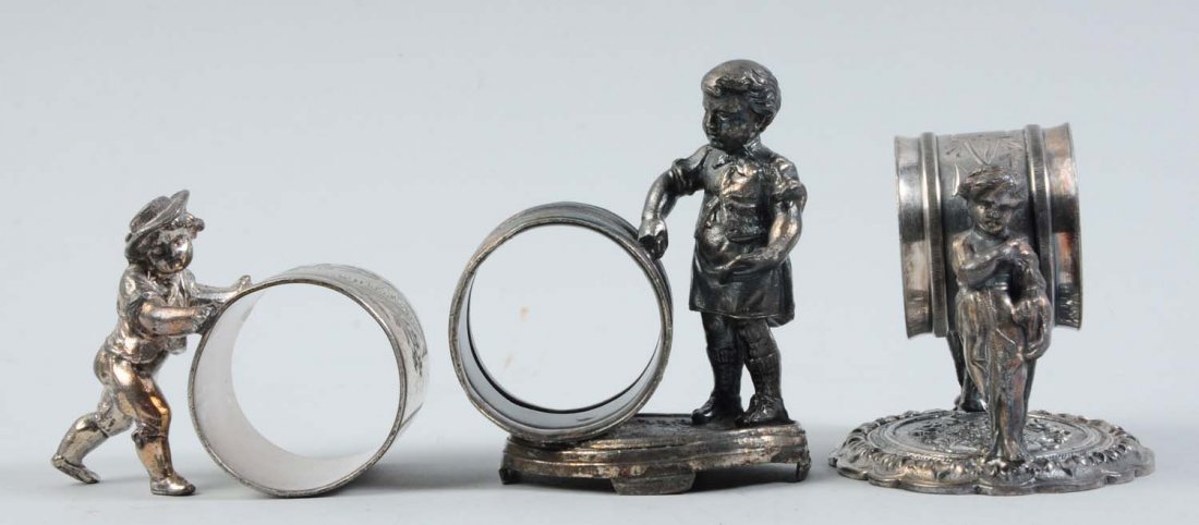 Lot of 3: Figural Napkin Rings.: This lot includes a napkin ring that has a young lad in a hat and knickers pushing the napkin holder. It is marked "Rogers Smith & Co., No. 161.", has some silver loss, but is still in good condition.
