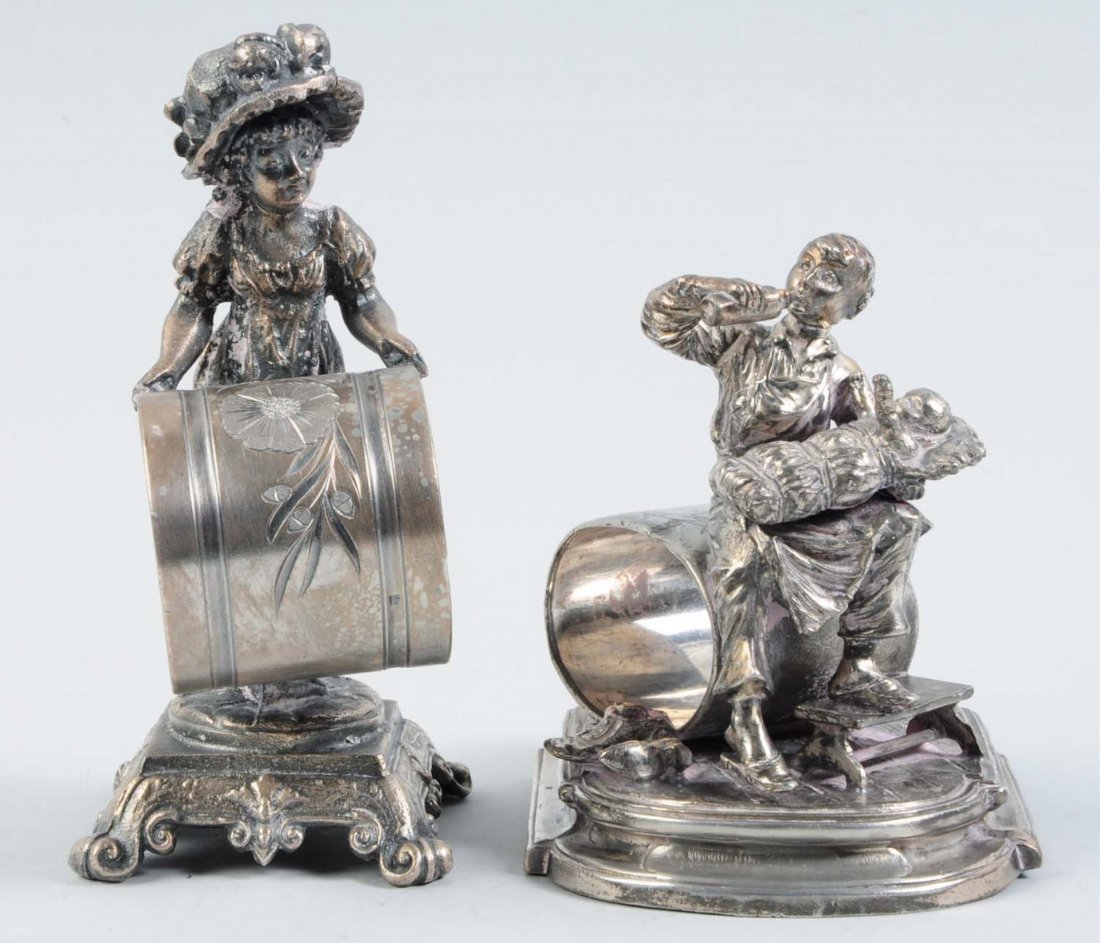 Lot of 2: Figural Napkin Rings.: The first napkin ring in the lot depicts a Kate Greenaway-type lady in a long gown and large bonnet standing on the small, fancy, square base, which has scrolled feet. She balances the napkin holder w