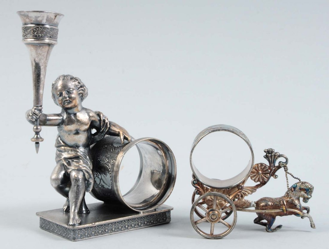Lot of 2: Figural Napkin Rings.: The lot includes a napkin ring that depicts a large draped cherub seated on a pedestal with one arm resting on the napkin holder. He is grasping a tall silver-plated bud vase base in his right hand. T