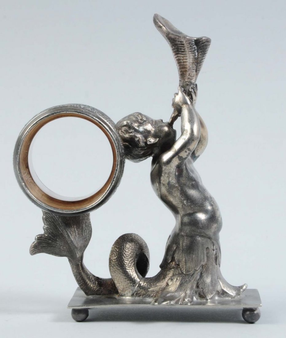 Figural Napkin Ring.: This napkin ring depicts Triton, the Greek god of the sea, blowing into a conch shell horn. The napkin holder is balanced on his head and tail. This example is on a rectangular base and is not marked.