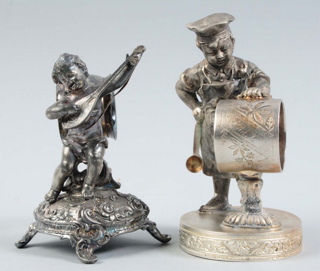 Lot of 2: Figural Napkin Rings.: This lot includes a napkin ring that has an extremely tall baker boy wearing a chef's hat and apron, and holding a spoon rest in his left hand on a napkin holder that is atop a pedestal. It is all on 