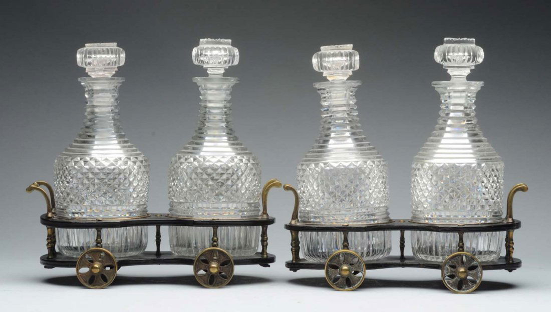 Pair of Papier Mache Decanter Trolleys.: 19thC, probably English, each with a black shaped base and upper section, mounted with metal handles, on four metal wheels, and with a set of four cut glass decanters. Metal mounts plated at one time.
