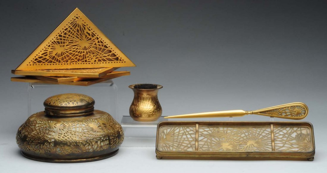 Tiffany Studios Pine Needle Desk Set.: Pen tray No. 1004, large inkwell with original insert No. 847, four blotter corners No. 997, letter opener No. 969, pen wipe with original brush No 982. There is wear to the gold and dents to the blot