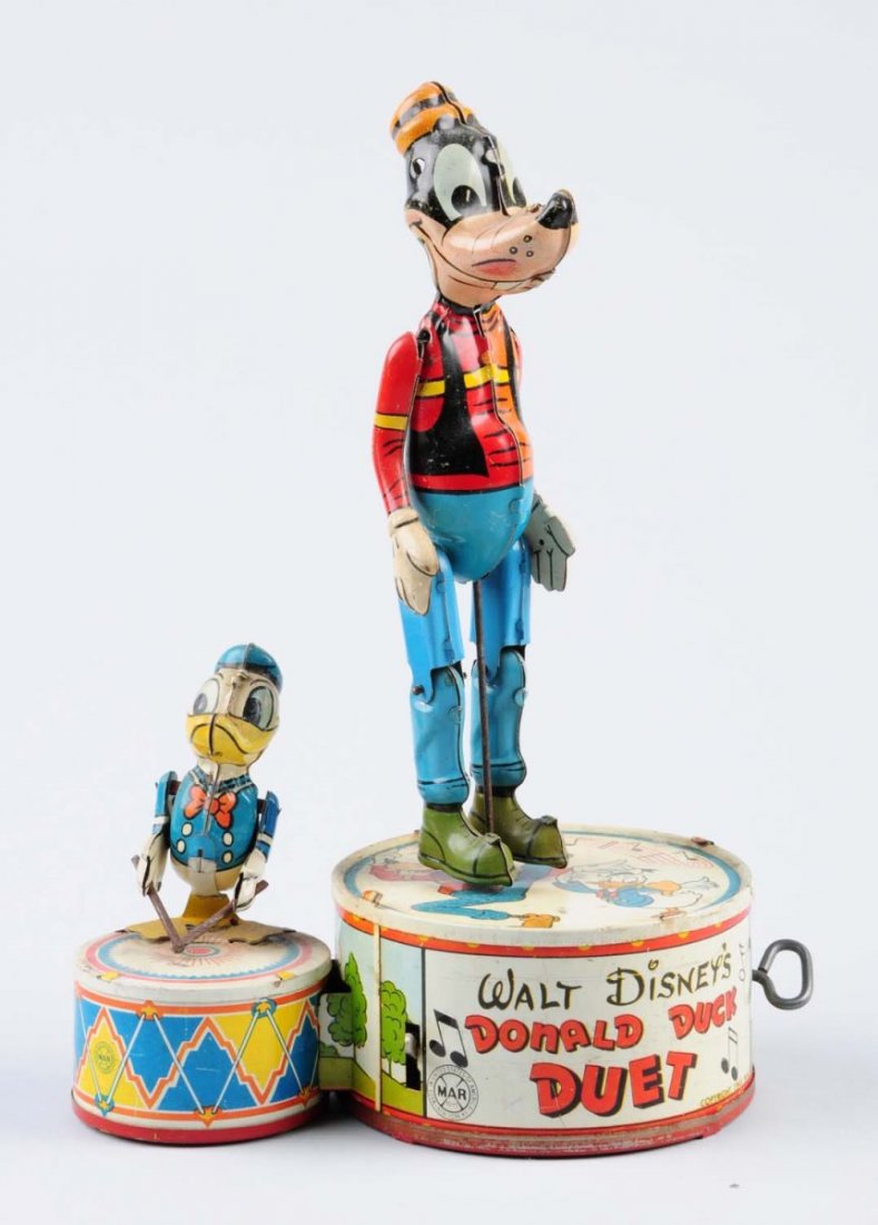 Marx Tin Wind-Up Donald Duck Duet Toy.: Depicts Donald Duck playing the drums and Goofy dancing. Some minor scratches and discoloration to the drum and the platform. Includes original key. Condition (Good - Very Good). Size 11" L.CORRECTION