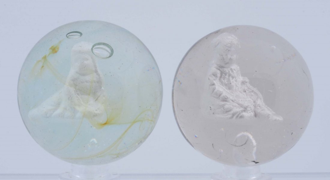 Lot Of 2: Human Figured Sulfide Marble.: The smaller is a girl in dress sitting holding an open book. The larger is a girl holding a mallet. Small fracture in figure near front arms. Both marbles have been polished. Size 1 - 11/16" to 1 - 3/