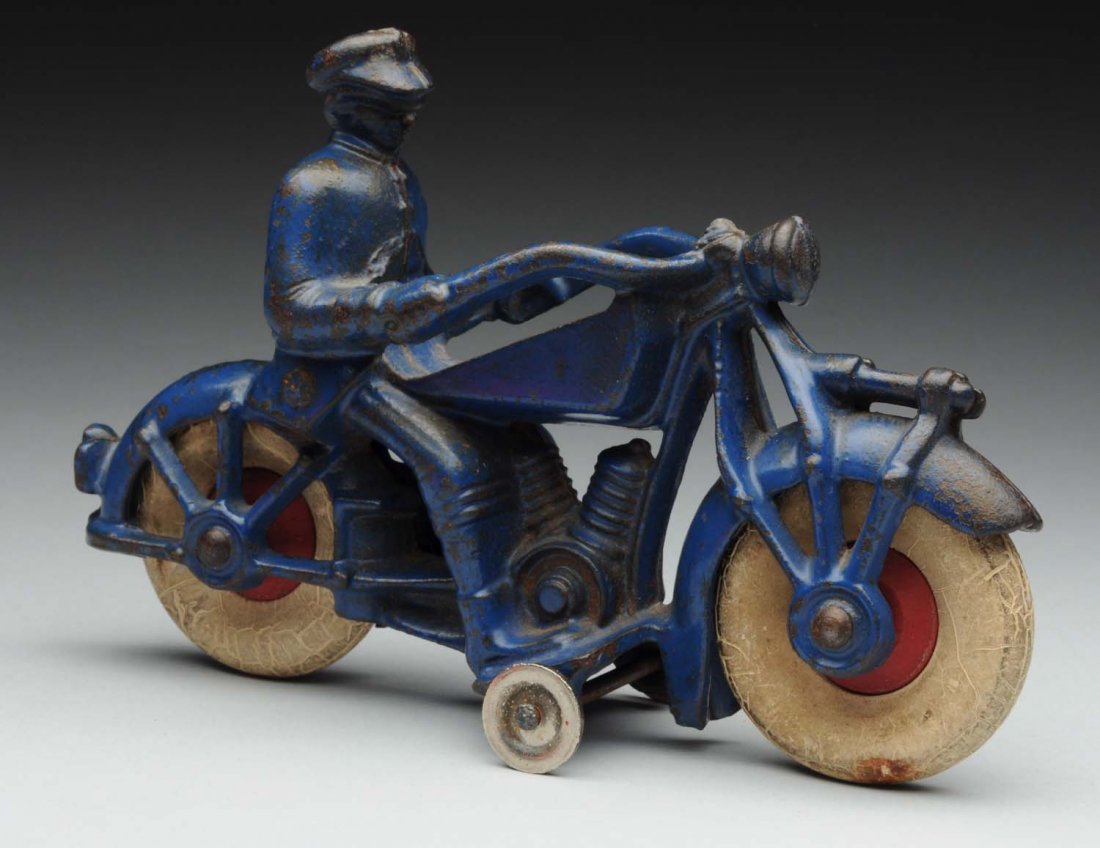 Cast Iron Champion Police Motorcycle Toy.: Has original white rubber tires, metal guide wheels on bottom. Police man riding motorcycle, has original red wooden hubs. Has some paint chipping and wear throughout. Condition (Very Good). Size 7" L