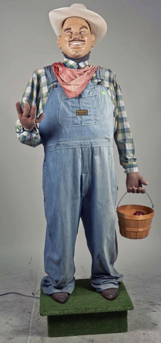 Life Size Migrant Worker Automaton Statue.: Male figure wearing jean overalls, plaid shirt, red bandana, white cowboy hat, and holding basket filled with apples, on base. Condition (Excellent). Size 72" T.