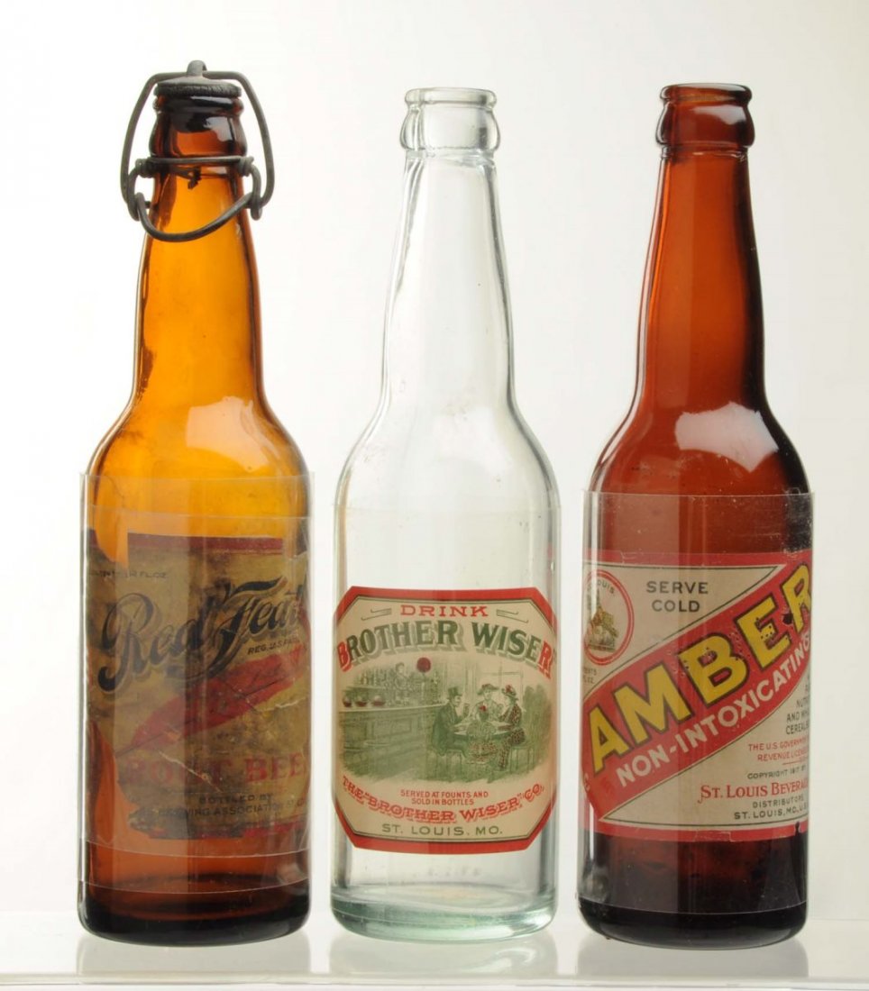 Lot Of 3: Prohibition Era Beverage Bottles.: With labels. This lot includes a bottle with an Amber Non-Intoxicating label, a bottle with a Red Feather Root Beer label, and a bottle with a Brother Wiser label. The Red Feather label has heavy loss