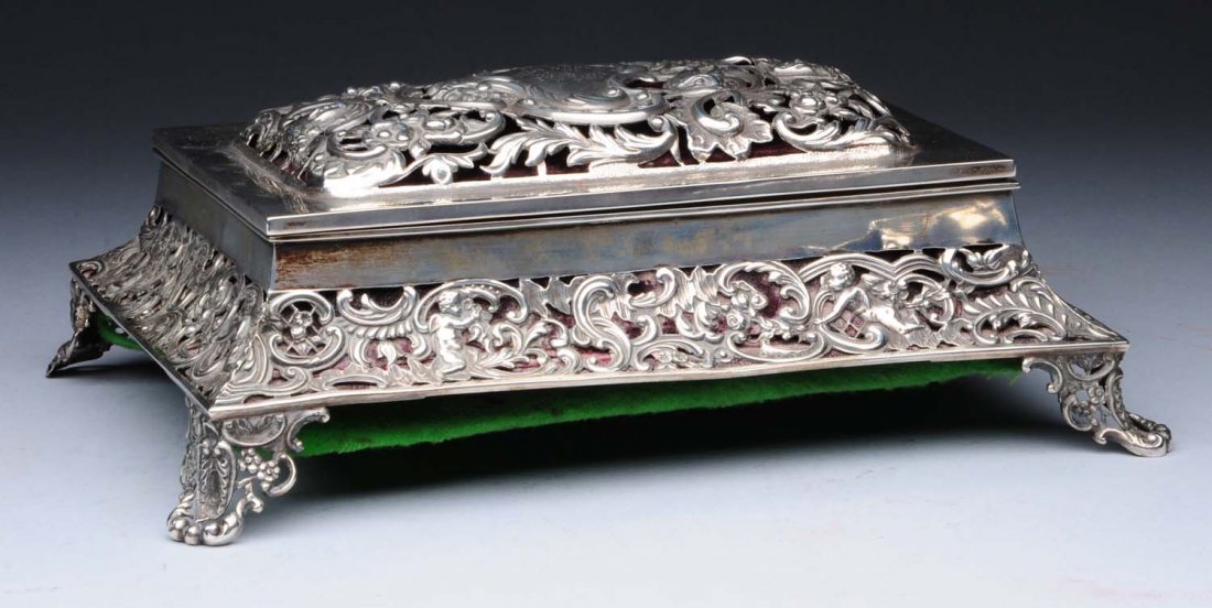 English Silver Jewellery Box.: London 1896 Wm. Comyns, rectangular with a domed hinged lid, fitted velvet-lined interior, and incurved sides pierced and chased with foliage and scrolls, the rims and sides plain. Length: 8-1/2 in - 