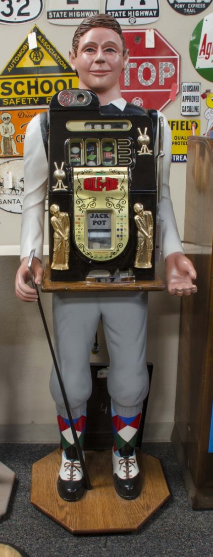 25 ¢ Mills Half Top Slot Machine In Golfer Stand: This floor model machine is housed in a carved wood stand shaped like a male golfer wood carving by Dick Delong. Slot machine features front jackpot and golf theme reels. Includes keys. Condition (Ver