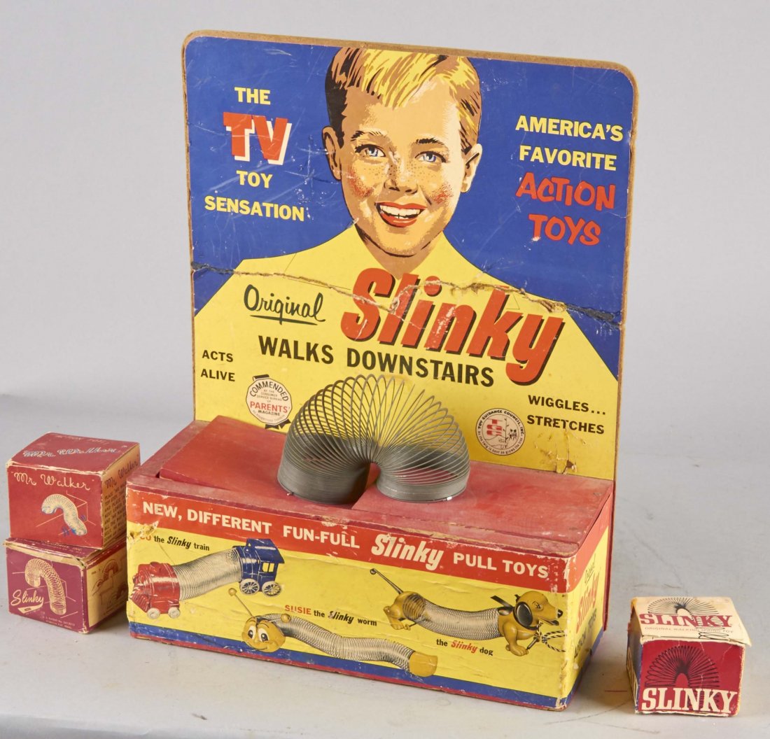 1957 Kinetic Slinky Display With 4 Toys: Including 1 moving Slinky attached to display (rock the left side of display with your fingers). Backboard has been repaired. All four sides of display have colorful graphic. Front and back show other