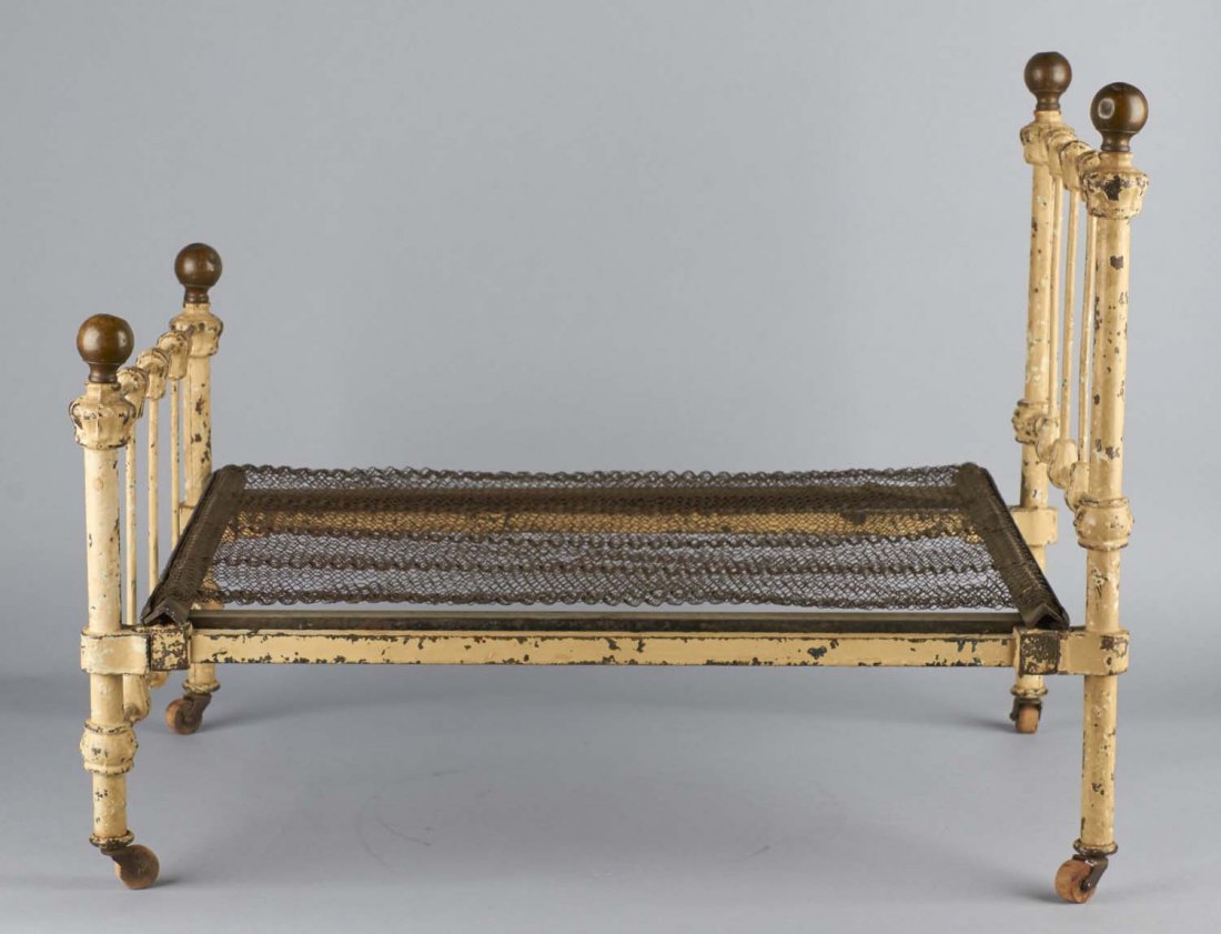 Metal Victorian Era Doll Bed: Antique painted metal mini bed on wooden wheels, with box spring base and brass balls on bed posts. Disassembles. Mattress rails are marked; Art bed Co. Chicago. In original condition and has paint we