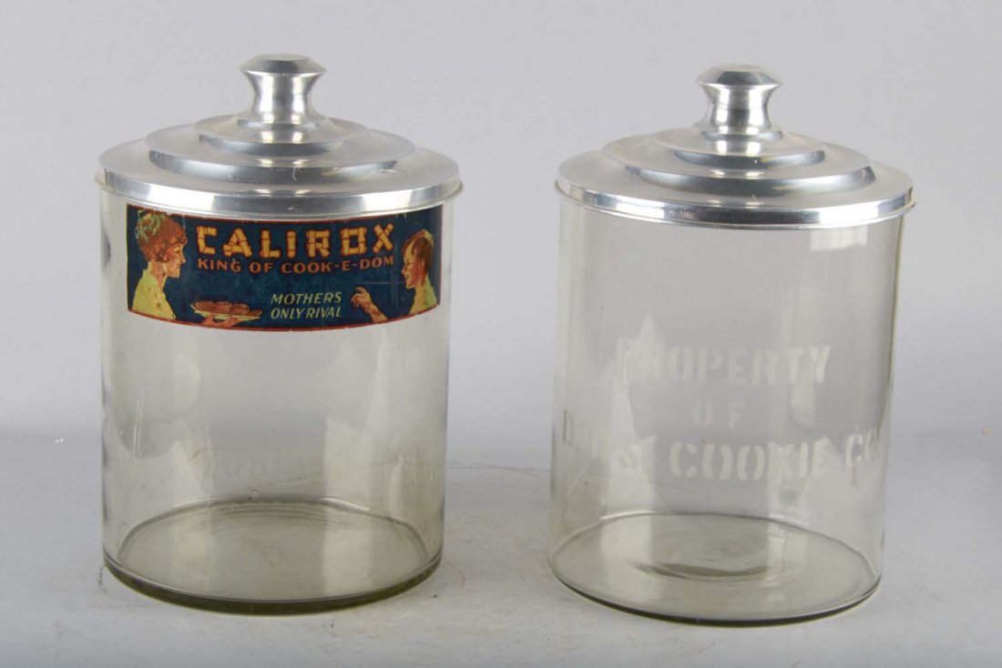 Lot of 2: Large Glass Cookie Jars: Lot of two large glass cookie jars with metal lids. Including 1 - glass cookie jar with decal reading "Calirox, King of Cook - E - Dom. Mothers only rival." Metal lid is stamped "Calirox Co." and 1- g