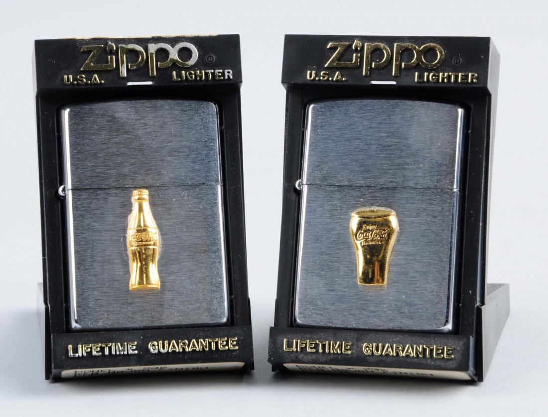 Pair Of Coca-Cola Zippo Lighters.: This lot includes two Zippo Coca-Cola lighters. One depicts a bottle and the other depicts a glass. Both are in original boxes and in great condition. Condition (Excellent). Size Each : 3" L.