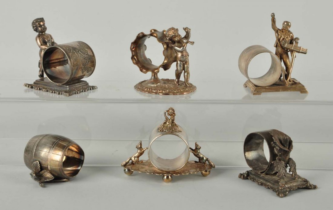 Lot Of 6: Figural Napkin Rings.: This lot includes a wingless cherub that tiptoes on one foot with the other foot in the air, as if dancing. The raised rectangular base has an acanthus leaf border. Marked Middletown Plate Co., #73. S