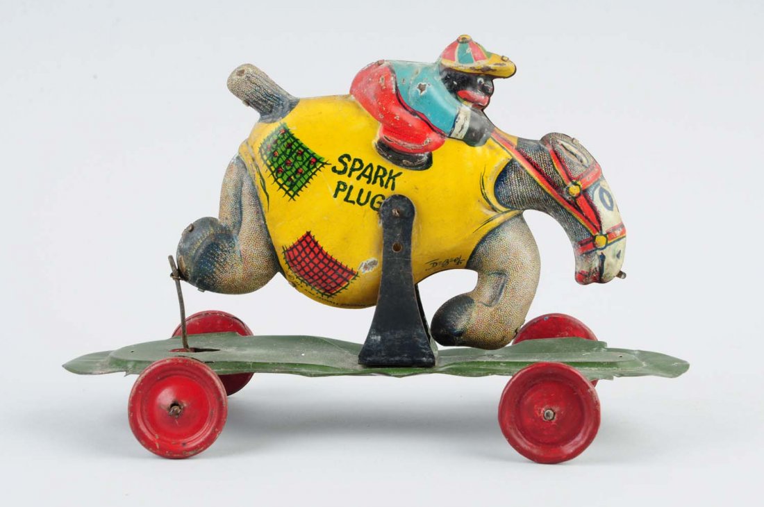 German Nifty Tin Litho Spark Plug Platform Toy.: African American rider riding a spark plug on the platform. When pulled, rider goes up and down. Some bending to platform. Front two wheels are replacements. Condition (Good - Very Good). Size 9'' L.