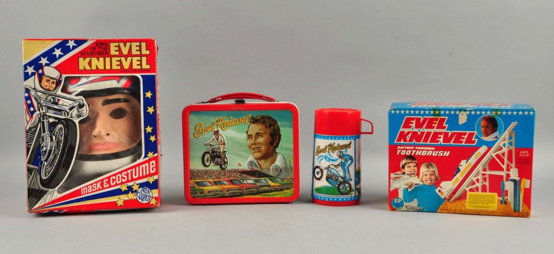 Lot Of 3: Vintage Evel Knievel Items.: A battery powered toothbrush, marked "Kenner", unused. A Halloween Costume, marked "Ben Cooper 1974" with some rubbing on the nose and a Lunchbox, marked "Aladdin Industries 1974", includes the thermo
