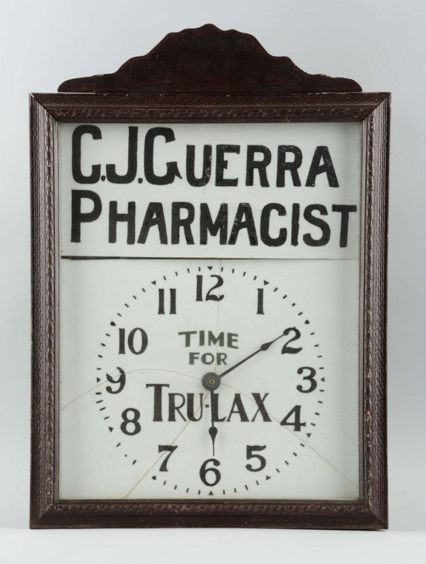 C.J. Guerra Pharmacist Advertising Clock.: This is a milk glass advertising clock in a wooden frame. The bottom section of the milk glass has four prominent cracks from the center to the edges of the piece. There is some paint loss on a few nu