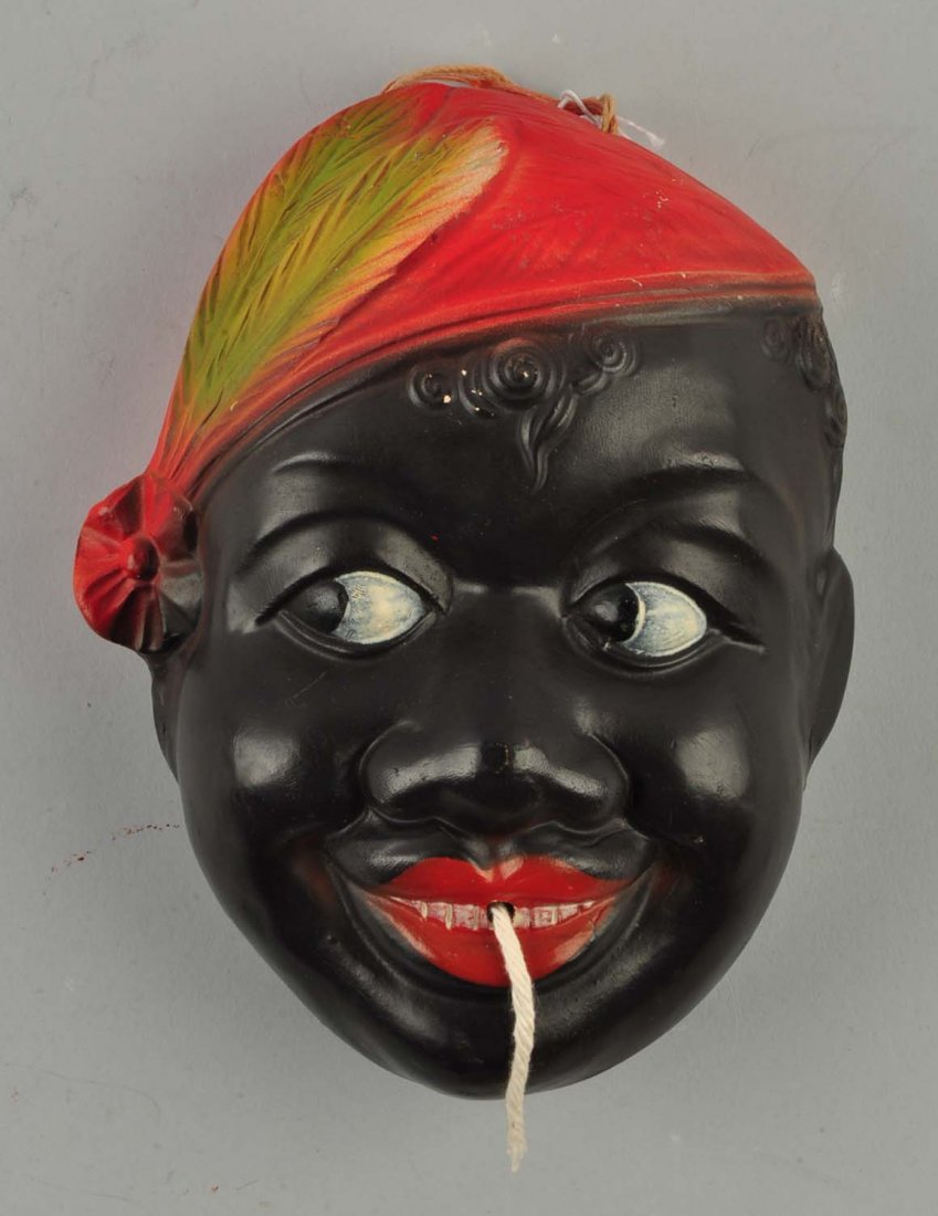 Black Americana Chalkware String Holder.: This lot is of a Black Americana chalkware string holder of a boy with curly hair and a red cap with green feathers. The string comes out of his mouth via a hole in one of the teeth. Scratches are pre