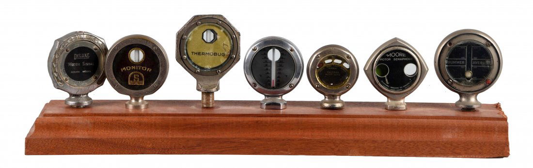 Lot of 7: Moto Meters.: Includes: Moore, Brennan, Deluxe, Monitor, Faberos, Messho and Thermobug. Mounted on a wood stand, there is some areas of corrosion. (Fair). 4" T.