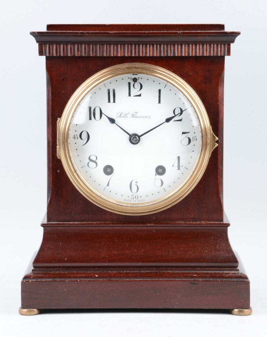 Seth Thomas "Wales" Mantle Clock: This lot is of a Seth Thomas "Wales" mantle clock. This clock has a dark wood rectangular shaped body with a white clock face and black numbers on the face. The clock’s face is protected by a glass