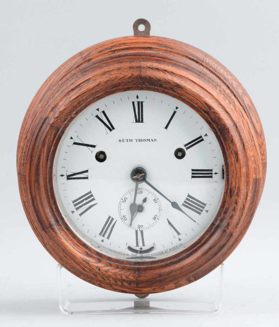 Seth Thomas Oak Wardroom Ships Clock: This lot is of a Seth Thomas oak Ships Bell “Wardroom” clock. This clock is comprised of an oak case with a white face and black Roman numerals. On the face of the clock, it is noted as being manu