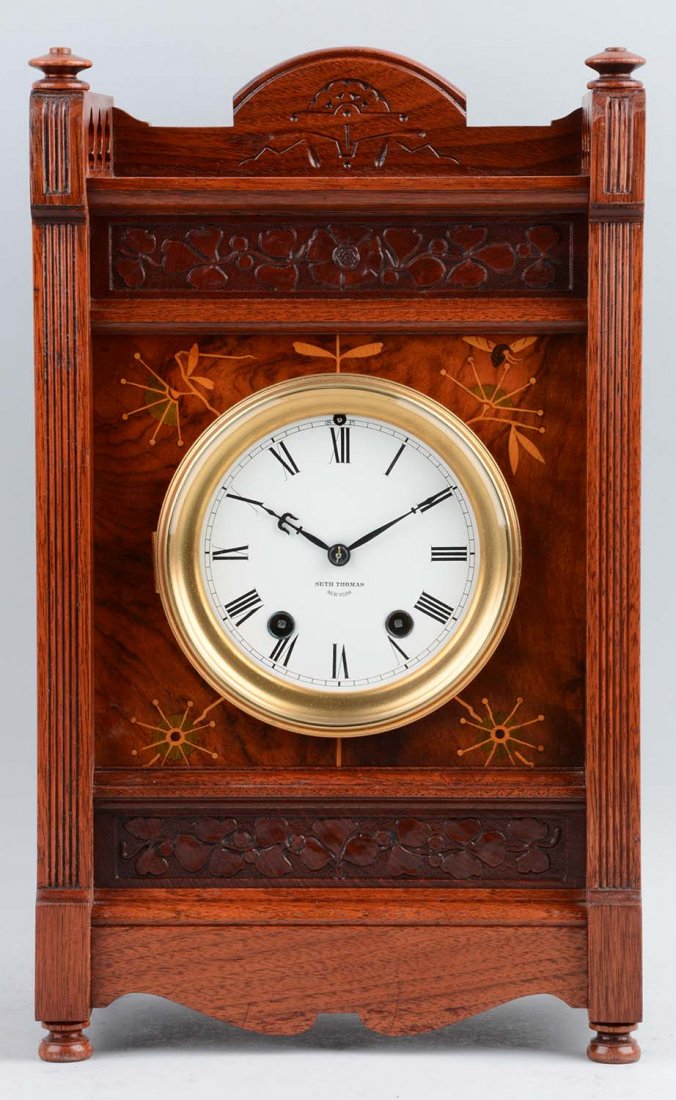 Seth Thomas "Bee" Clock: This lot is of a Seth Thomas "Bee" clock with inlay and carved motifs. On this rectangularly shaped clock, burled wood is in the middle surrounding the clock’s face. The inlay design is found within