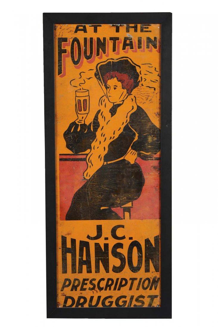 Ithaca Sign Works J.C. Hanson Prescription Druggist Tin: This single sided tin sign is housed in a contemporary black frame. Reads "At The Fountain" and shows a woman drinking a warm beverage at a soda fountain or bar. It has some minor scratches and oxidat