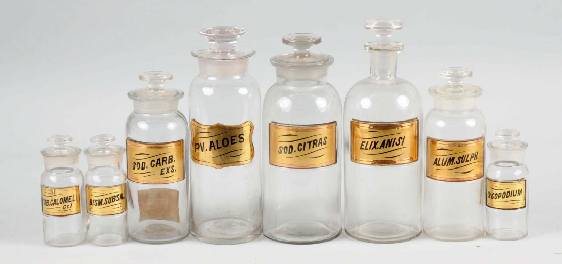 Lot of 8: Early Apothecary Jars.: All of the jars have ground necks and reverse glass labels. Some of the labels are titled: Elix.Anisi, Alum. Sulph., Pv. Aloes and others. (Very Good). Largest: 10" T.