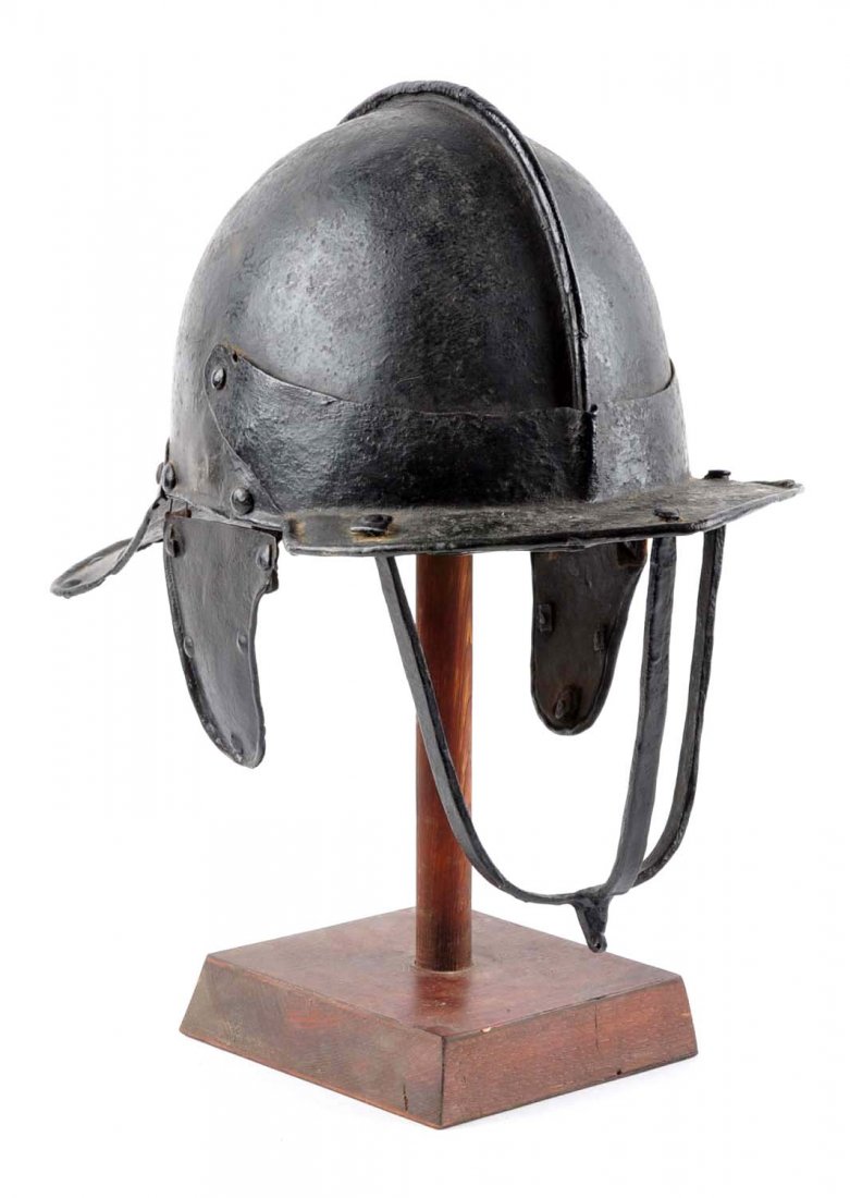 17th Century English Lobster Tail Burgonet.: Of blackened iron, one piece skull with ribbed lame neck defense with rolled edges and rivets. Cheekpieces with rivets and rolled rims. Pivoting brim and face defense composed of three forged iron bar