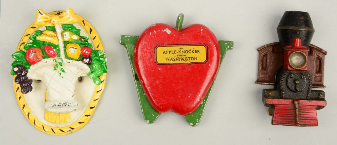 Lot of 3: Cast Iron Assorted Doorknockers: Includes Basket of Fruit, rare; Locomotive Engine, brass; and Souvenir Apple - Signed “An Apple-Knocker from Washington” (aluminum). (Excellent). Largest: 4" T.