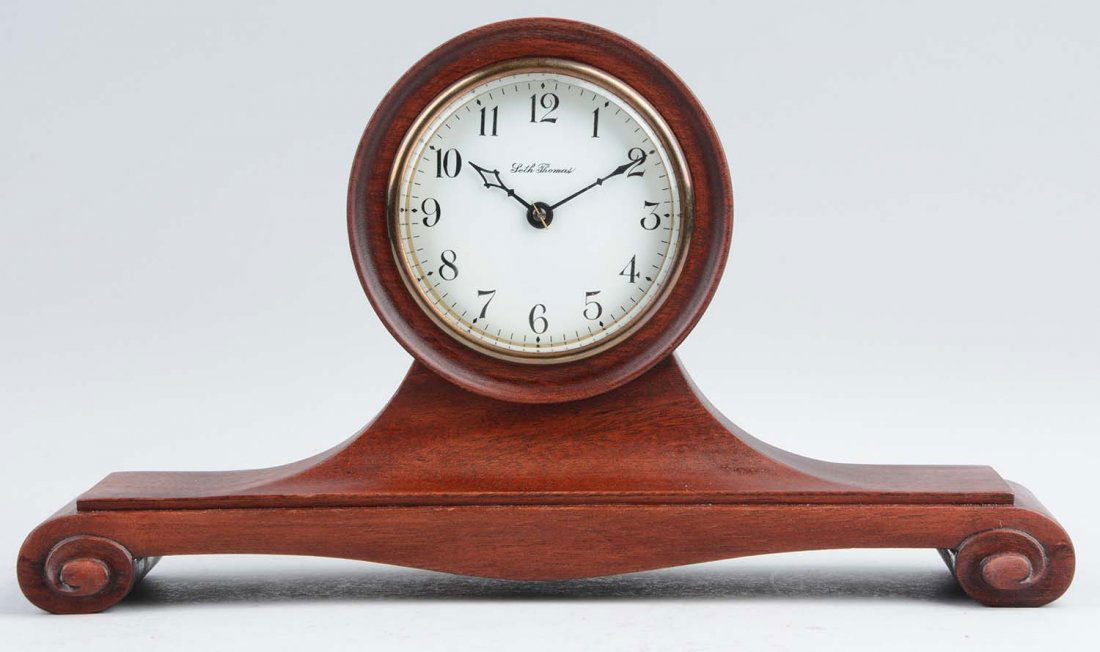 Seth Thomas Anson Clock.: This lot is of a Seth Thomas Anson clock. The clock is comprised of a medium colored wood body with a white face and black numbers. A very minimal crack is present on the face of the clock. Very Good-