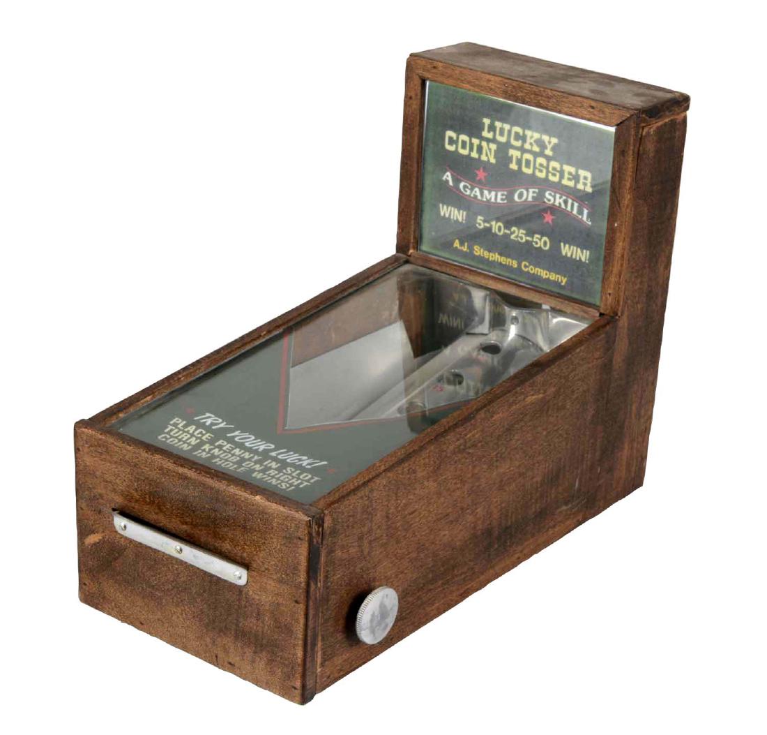1¢ A.J. Stephens & Co. Lucky Coin Tosser Counter Game: Player places their penny in the slot and turns the knob to flip their coin into one of the designated holes. The wooden cabinet shows wear and the paper signage appear to be modern and not original t