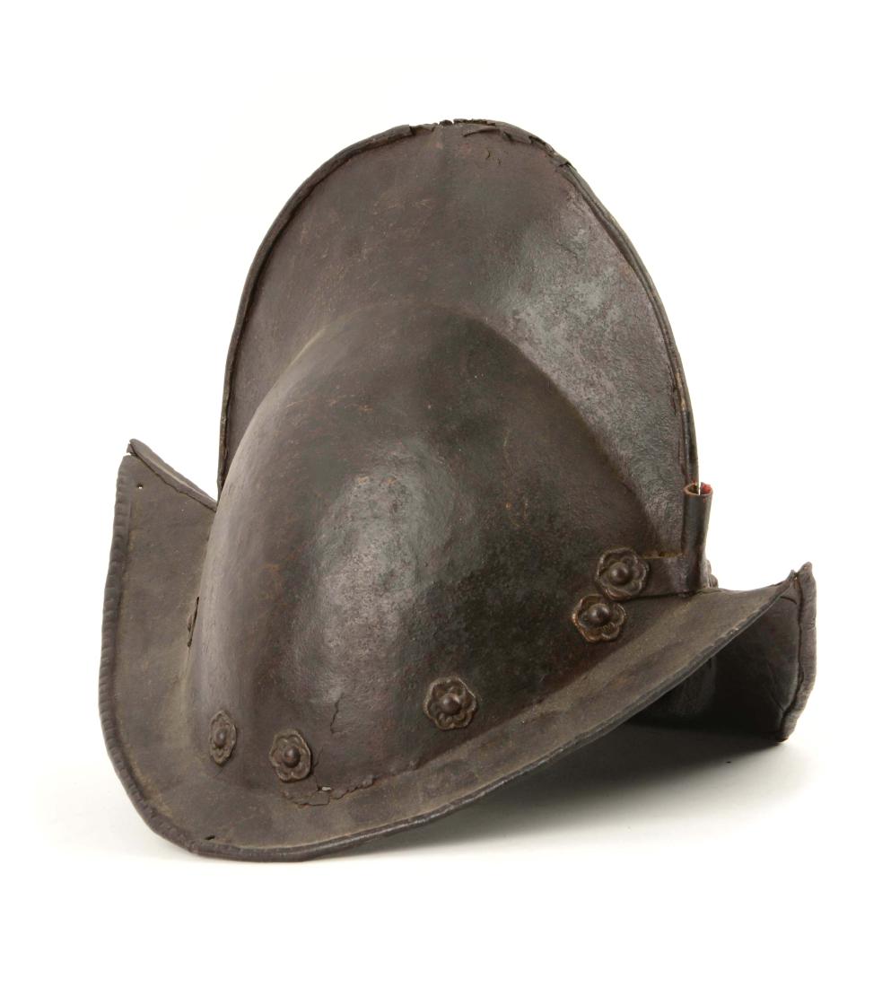 Morion helmet, probably Italian, circa 1570.: 1) Iron open headpiece with high comb and brim forming high peaks front and back and turned down at the sides. Edged turned in at rim. Plume socket attached in front at junction of brim and crown. Riv