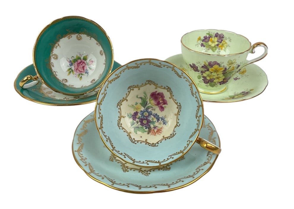 Aynsley Fine Bone China Tea Cups and Matching Saucers: Aynsley bone china teacups and matching saucers featuring floral and gold designs. Includes one light green set with purple and yellow floral patterns, one pale blue set with multicolor floral central