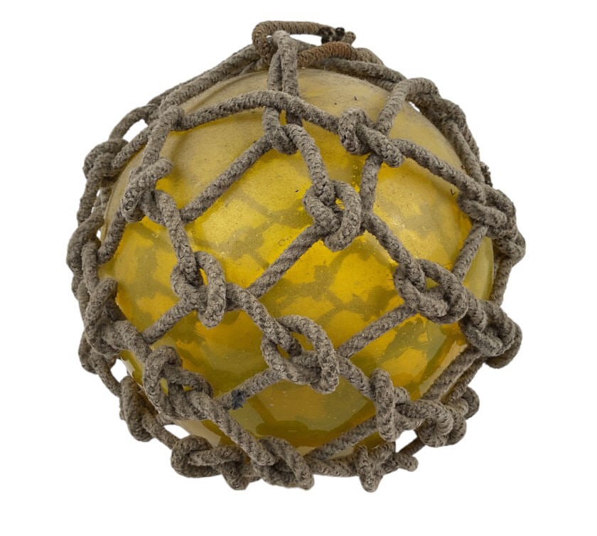 Yellow Glass Fishing Buoy Float with Rope Netting: Yellow glass fishing float encased in rope netting. The float features well-preserved glass with visable signs of handcrafted production. The rope netting is securely tied, showing natural aging and w