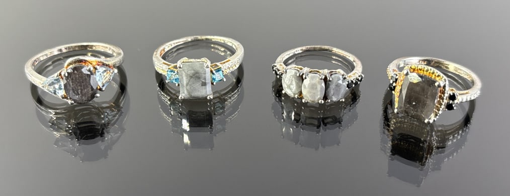 (4) 925 Sterling Silver Rings featuring Gray Gemstones. Total Weight: 11.78 grams: (4) 925 Sterling Silver rings featuring gray gemstones. Rings are sizes 9 and 7. The first ring features a rectangle-cut gray stone accented by blue stones. The second ring features an oval-cut gray s