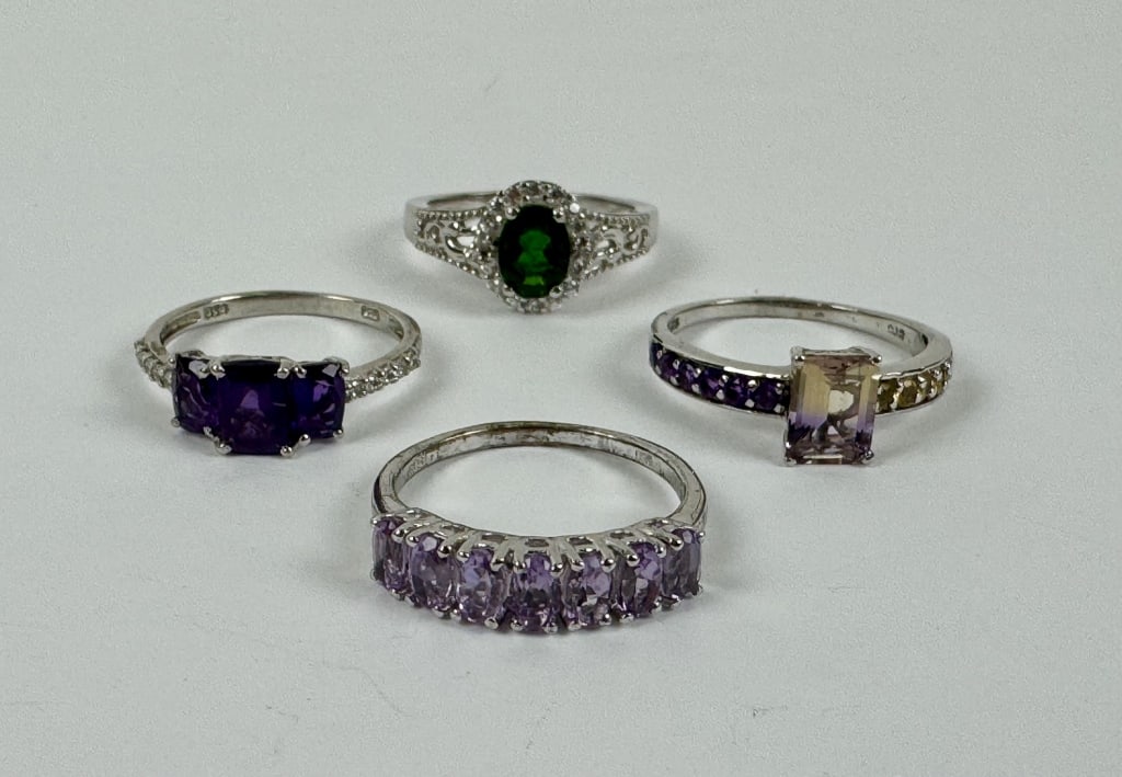 (4) 925 Sterling Silver Rings featuring Gemstones: TW: 12.22 grams. (4) 925 sterling silver rings featuring green and purple gemstones. Sizes 9 and 10. The first ring features an oval-cut green gemstone with clear gemstone accents. The second ring fea