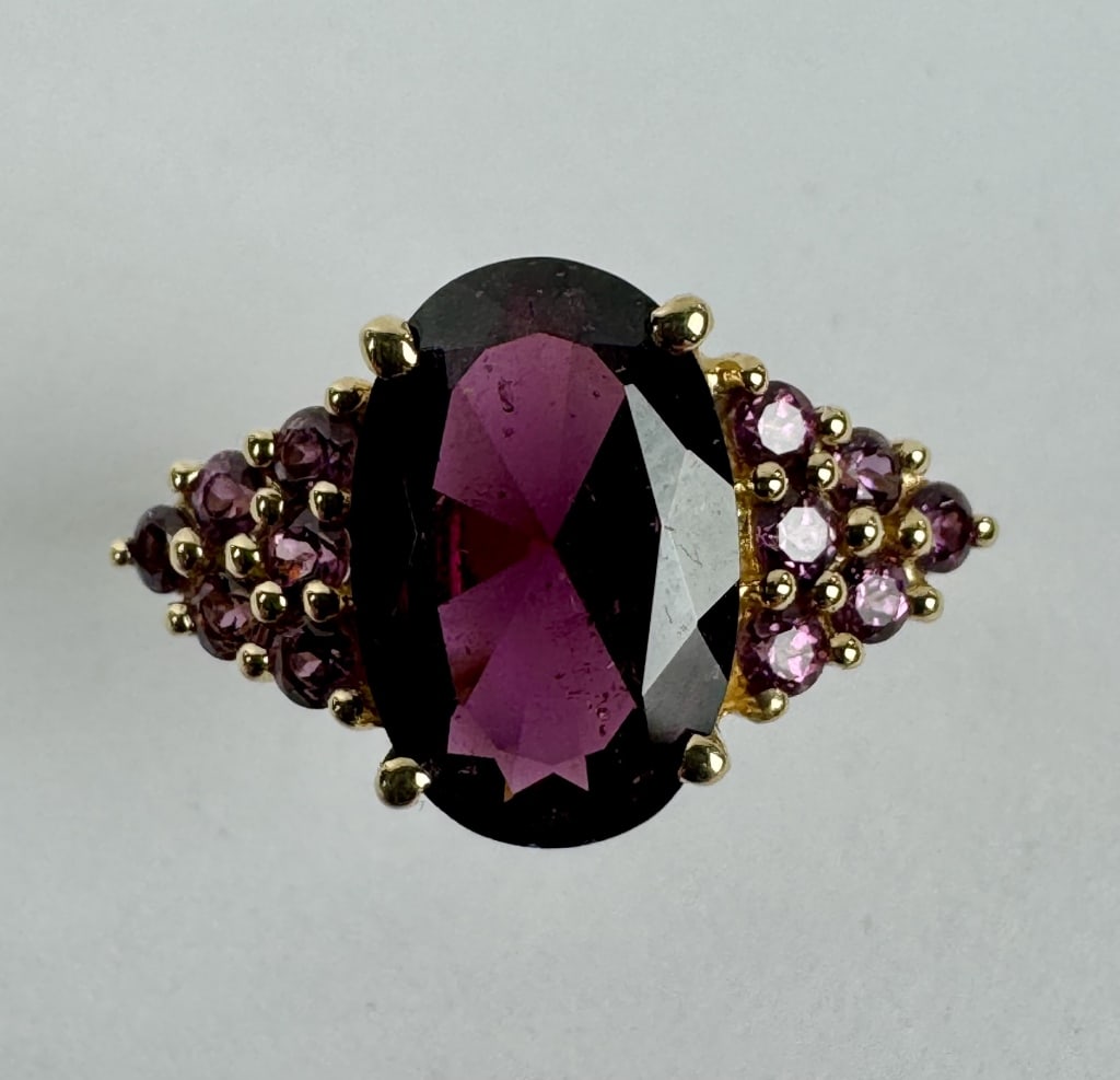 14K Gold Ring featuring a Dark Red Gemstone: TW: 3.25 grams. 14K Gold ring featuring a dark red oval-cut center stone with pink gemstone accents. Size 7.