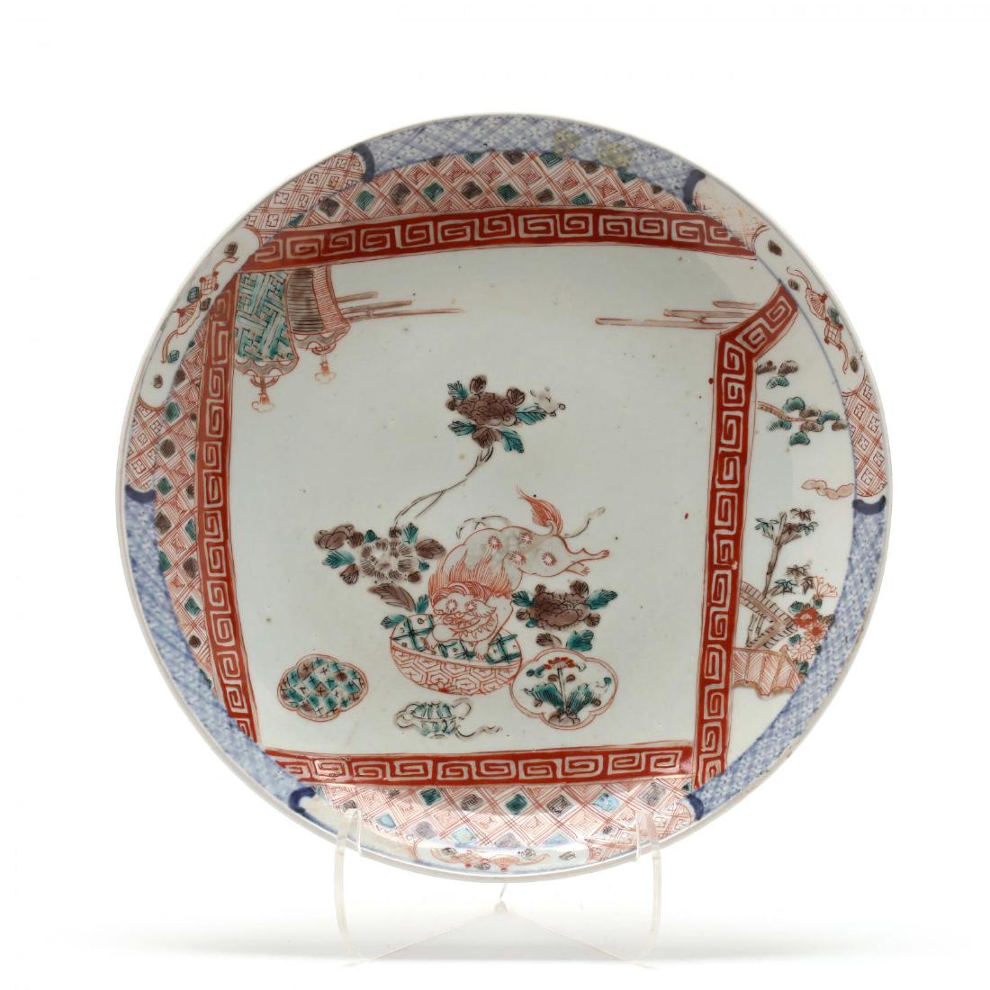 A Japanese Imari Charger: 19th century, enameled with a playful foo lion, within panels of red and blue foliage around the rim, painted around the exterior splashes of meandering tendrils, with three kiln spur marks on undersi