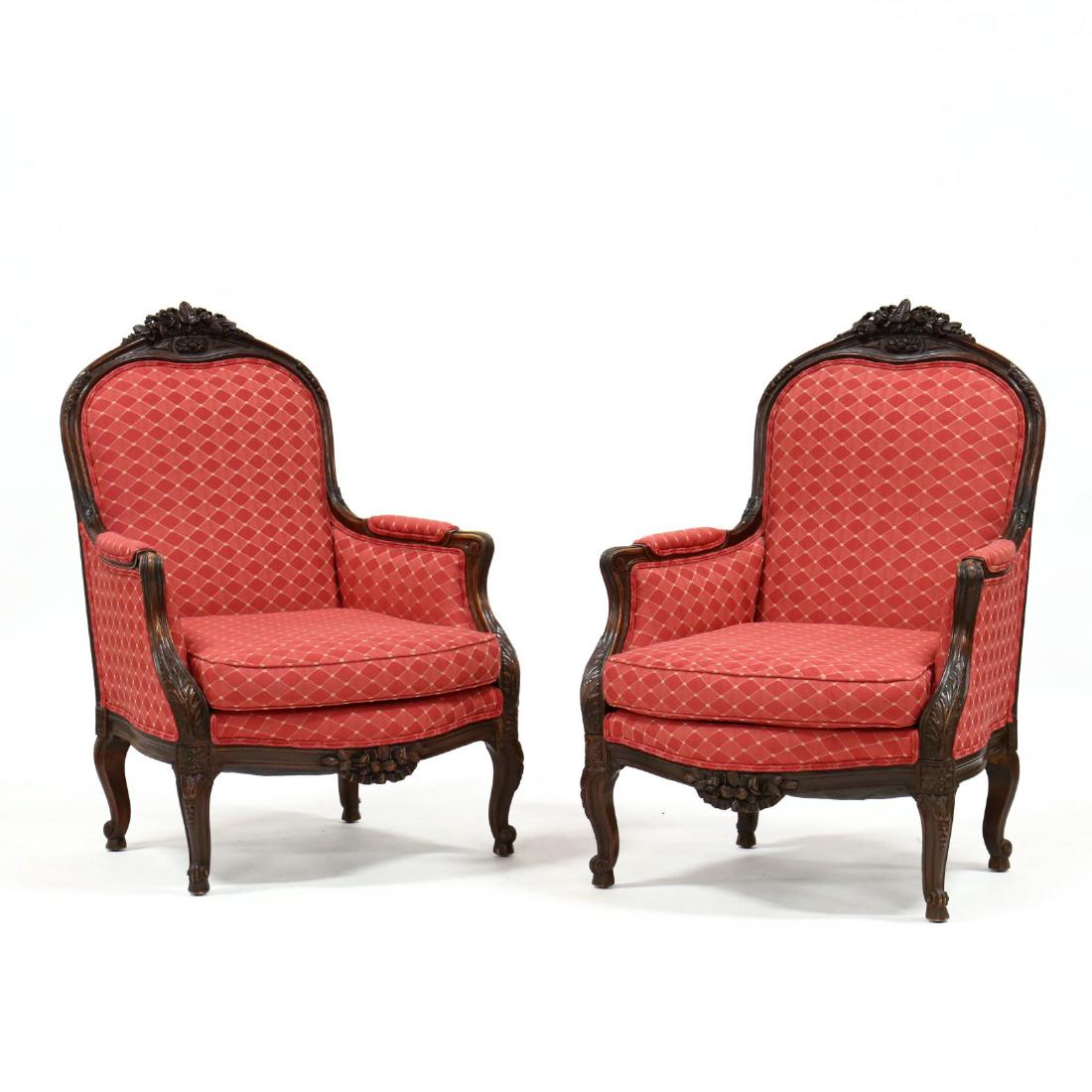 Pair of Louis XV Style Carved Bergeres: mid 20th century, walnut, crest rail with floral spray and ribbon, later red upholstery with slip seat, repeating floral carved skirt, on cabriole legs. 43 x 28 x 26 in. From the Collection of Mr. & M