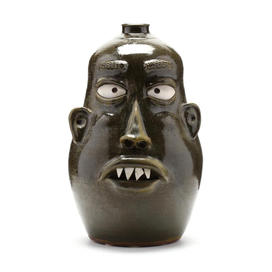 Georgia Folk Pottery, Wayne Hewell: Gillsville, Georgia, a giant face jug with frogskin glaze, unglazed eyes, pointed china plate teeth, short strap handle, signed on the bottom in script and dated 2004. 18 x 9 in. Additional high-resol