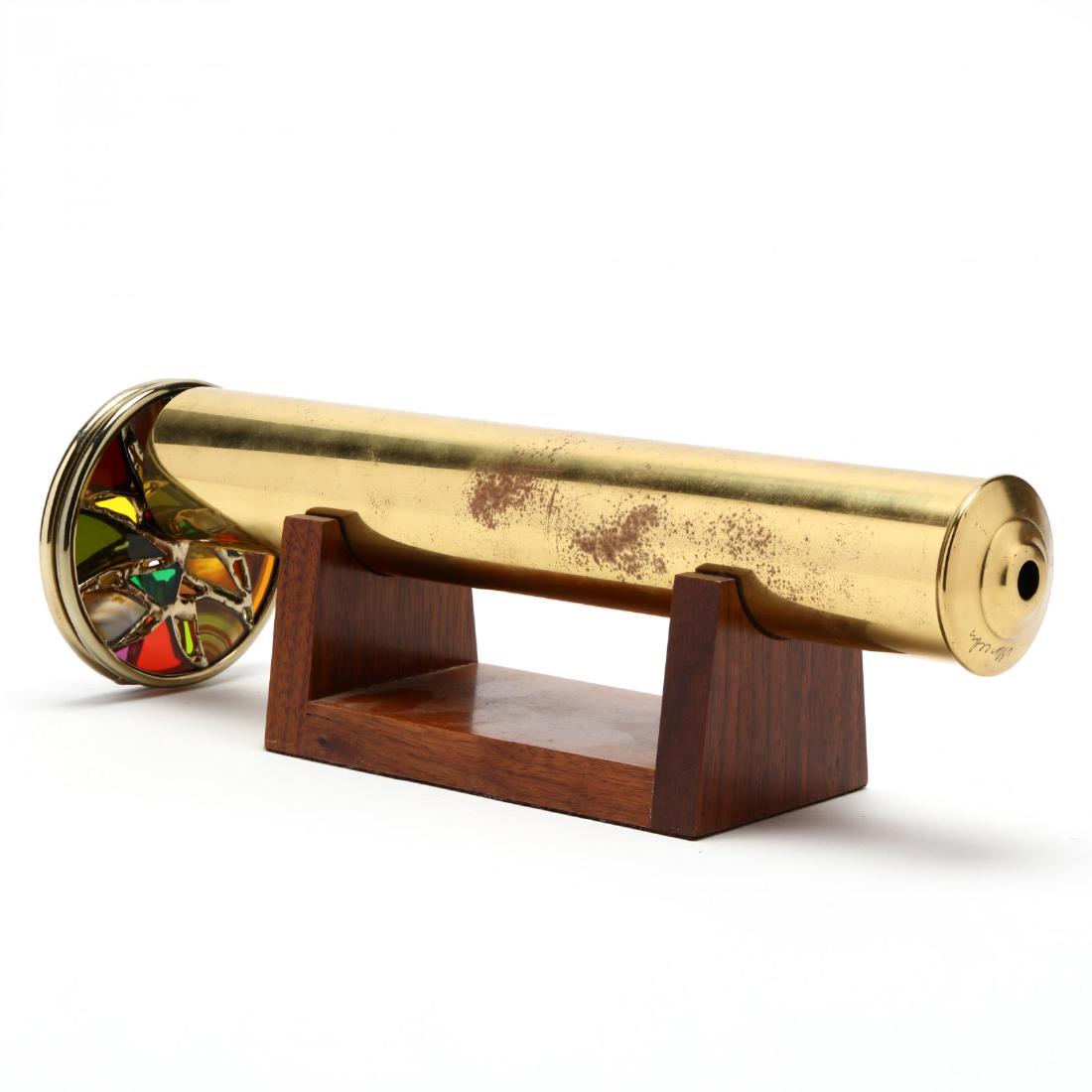 Artist Signed Brass Wheel Kaleidoscope: 20th century, brass body with a double wheel viewer composed of agate and colored glass, presented on wooden stand. HOA 4.5 x 12.5 in. From the Collection of Charlotte Rodman, Southern Pines, NC Charl