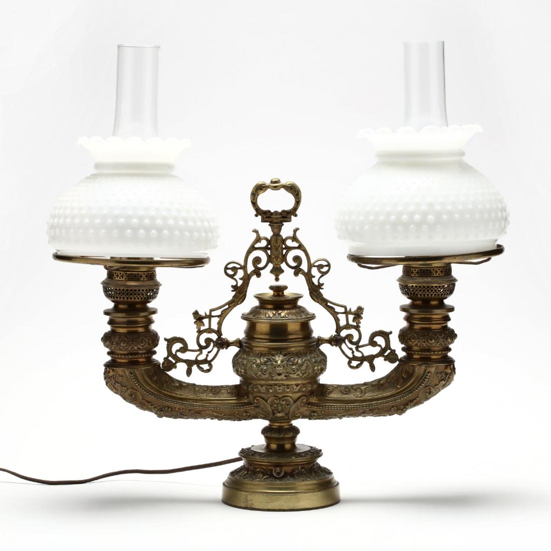 Plume & Atwood "Harvard" Double Arm Student Lamp: fourth quarter of the 19th century, marked to burner adjustments, electrified, heavy cast brass frame with decoration in the Renaissance Revival style, with later glass hurricane shades and milk glass