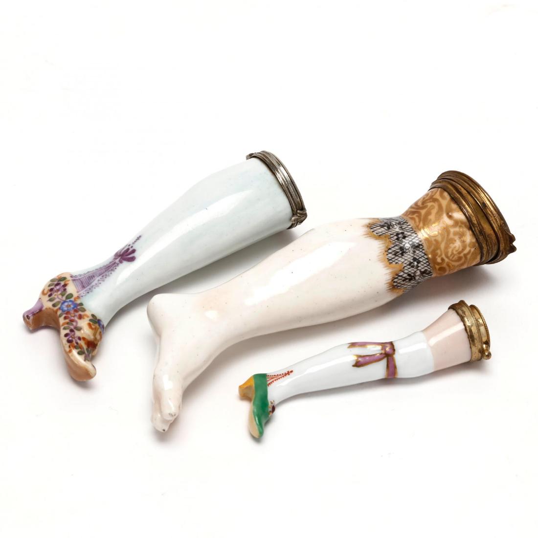 Three Porcelain Needle Cases with Metal Mounts: each in a lady's leg motif with hand painted detailing, two with gilt metal mounts and one with a silver tone metal mount, the smaller with blue underglaze maker's mark. 2.5 in.; 3 in.; 4 in. Additio