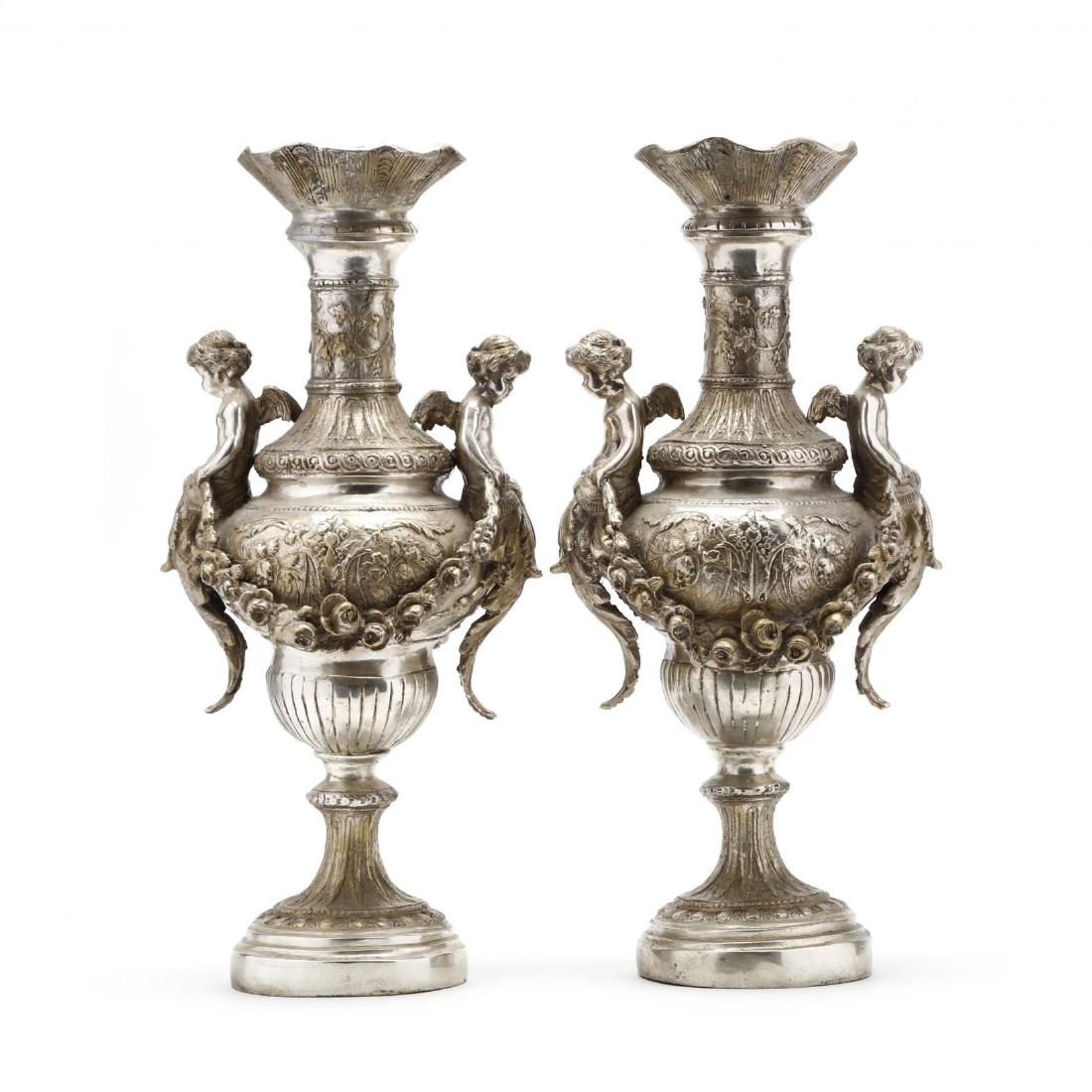 A Pair of Silvertone Renaissance Revival Style Urns: A Pair of Silvertone Renaissance Revival Style Urns 20th century, each with putti perched on body of vase and holding floral swags, the urns are cast with grapevine motif to body and neck, unmarked. 1