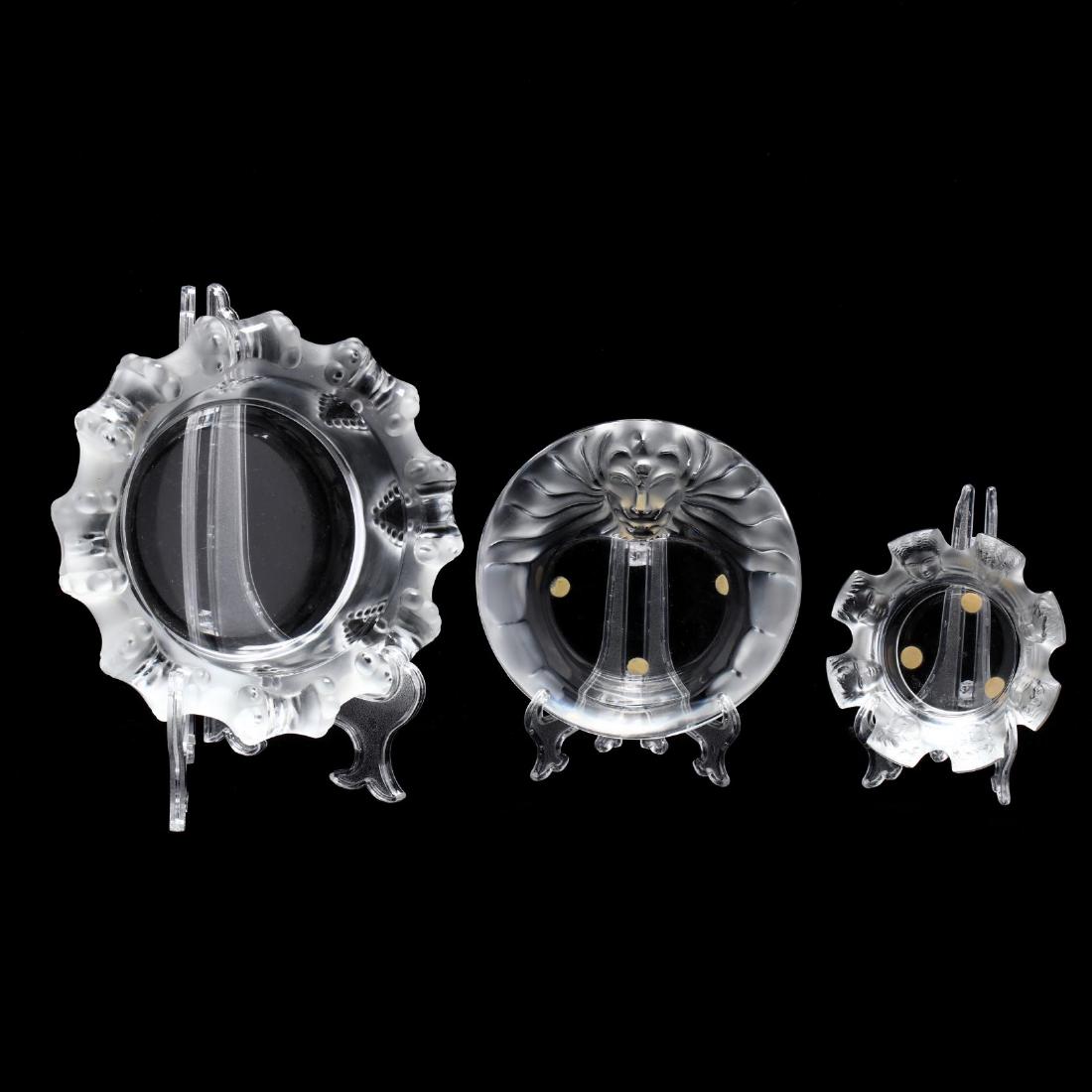 Three Lalique Ash Trays: Three Lalique Ash Trays France, late 20th century, including "Tete de Lion", "St. Nicholas", and "Cannes", each in clear frosted and polished crystal, signed. Largest 2.5 x 8 in. diameter. The Estate 