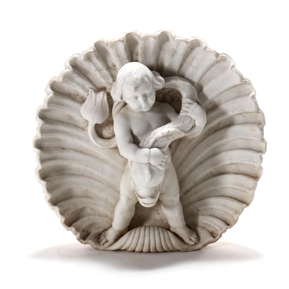 Italian Carved Marble Fountainhead: Italian Carved Marble Fountainhead early 20th century, standing putto holding a dolphin, within a carved shell, fountain hole and spout from verso to dolphin's mouth. 15.5 x 17 x 5 in. From the Collec