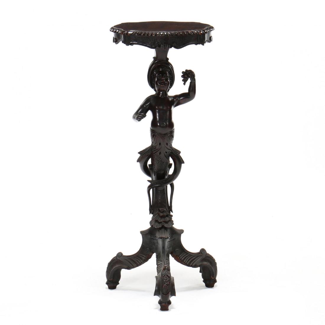 Venetian Carved Figural Stand: Venetian Carved Figural Stand second half of the 19th century, mixed hardwood, shaped top with gadrooned border, stylized putto with acanthus leaf and vine base, chip carving, rosettes, and shell, tri